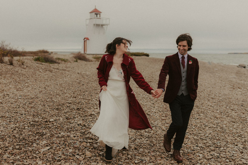 Bride and groom holding hands by the lake at the Hecla Lighthouse during their wedding day.